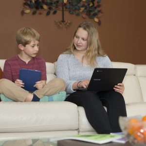 Children on couch with tablet and computer, working on tutoring homework