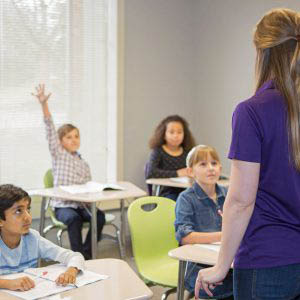 Student in tutoring class raising hand; academy teacher instructing small classroom